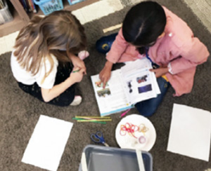 Two students sitting on classroom floor looking at a book