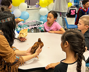 Adult holding a live chicken at a classroom table with young students 